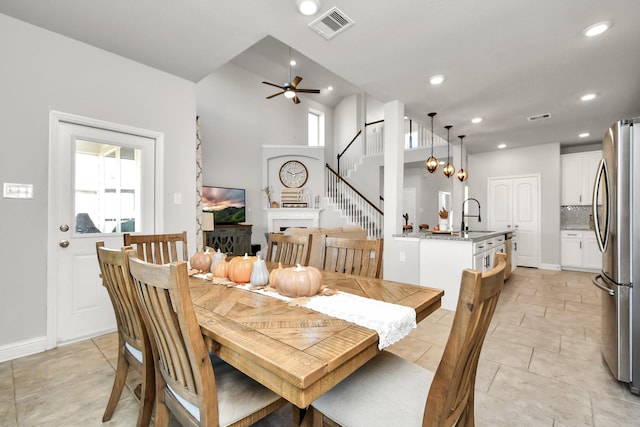 dining area with sink, ceiling fan with notable chandelier, and a towering ceiling