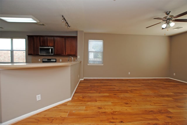 kitchen featuring range, light wood-type flooring, track lighting, kitchen peninsula, and ceiling fan