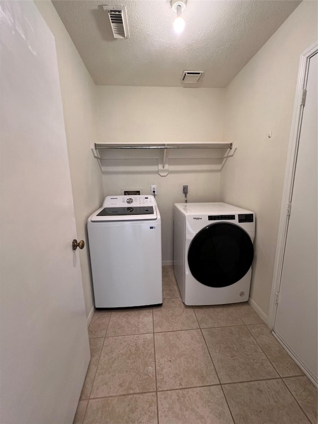 clothes washing area featuring laundry area, light tile patterned floors, visible vents, washing machine and clothes dryer, and a textured ceiling