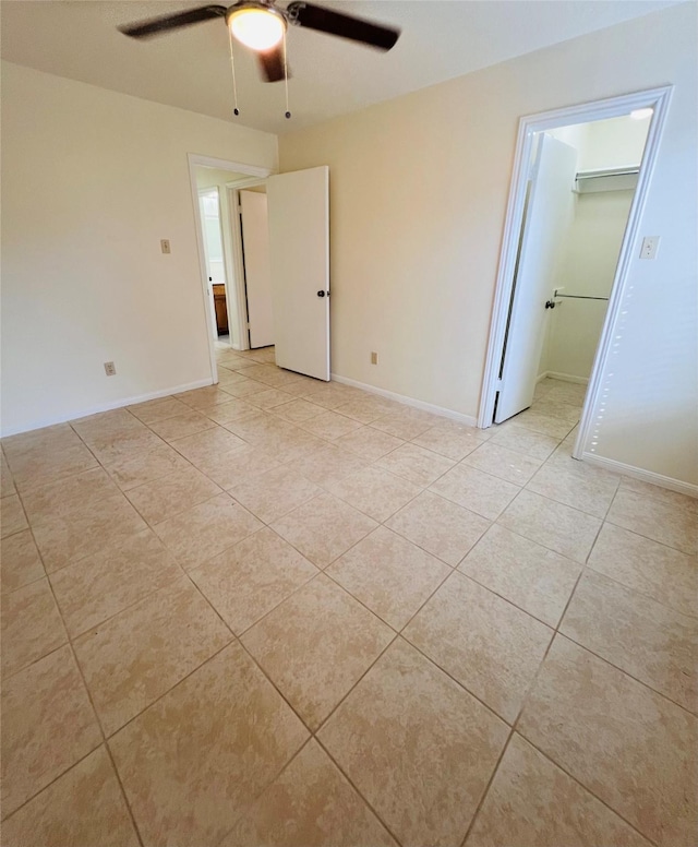 unfurnished bedroom with light tile patterned floors, a spacious closet, ceiling fan, and baseboards