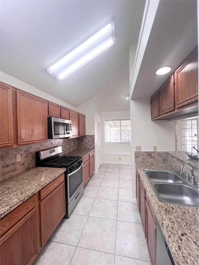 kitchen featuring tasteful backsplash, appliances with stainless steel finishes, brown cabinetry, vaulted ceiling, and a sink