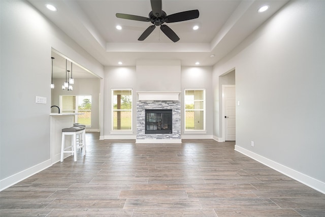 unfurnished living room with a raised ceiling, ceiling fan, and a fireplace