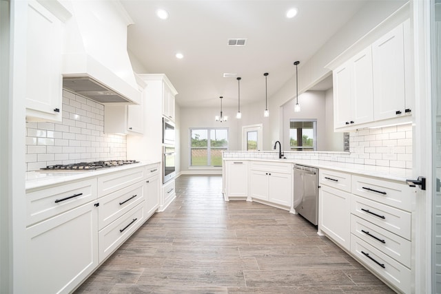 kitchen featuring white cabinetry, custom exhaust hood, hanging light fixtures, kitchen peninsula, and stainless steel appliances