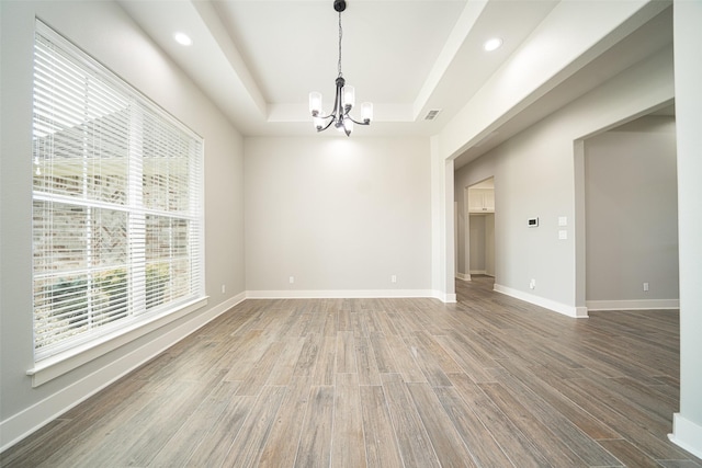 empty room featuring an inviting chandelier, wood-type flooring, and a raised ceiling