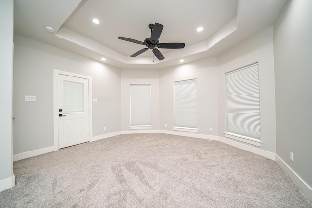 empty room with light carpet, a raised ceiling, and ceiling fan