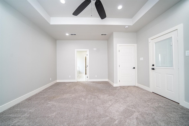 unfurnished room featuring light carpet, a tray ceiling, and ceiling fan