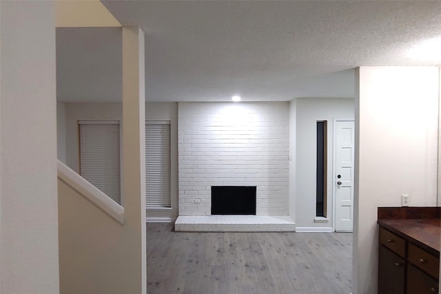 unfurnished living room featuring a brick fireplace, light hardwood / wood-style floors, and a textured ceiling