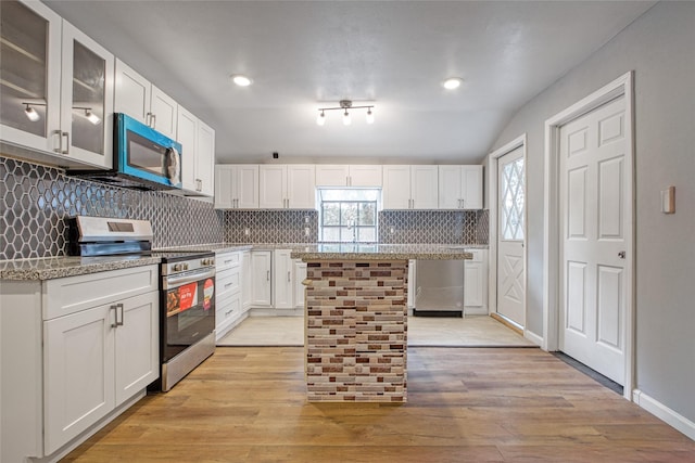 kitchen with stainless steel electric range oven, white cabinetry, light stone counters, a kitchen island, and vaulted ceiling