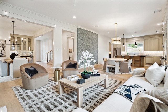 living room with an inviting chandelier, ornamental molding, sink, and light hardwood / wood-style floors