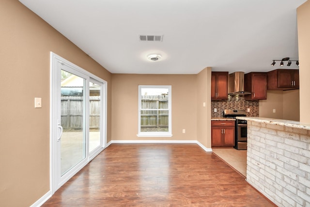 kitchen featuring wall chimney exhaust hood, wood-type flooring, stainless steel stove, light stone countertops, and decorative backsplash