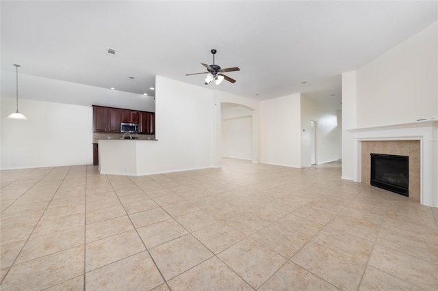 unfurnished living room with ceiling fan, a tile fireplace, and light tile patterned floors