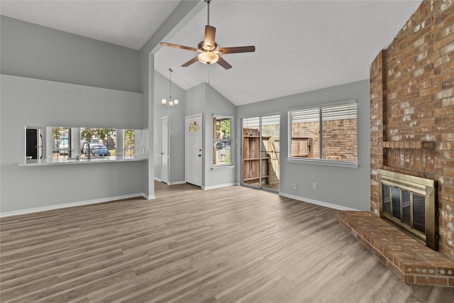 unfurnished living room with a healthy amount of sunlight, a fireplace, light hardwood / wood-style floors, and ceiling fan with notable chandelier