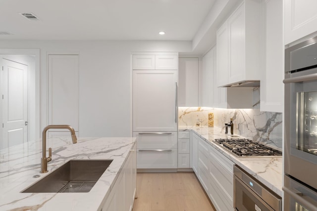 kitchen featuring light stone counters, white cabinetry, and sink