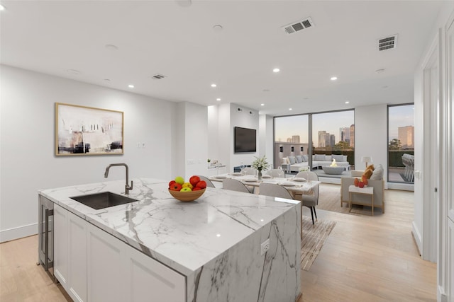 kitchen with white cabinetry, a kitchen island with sink, light stone countertops, and sink