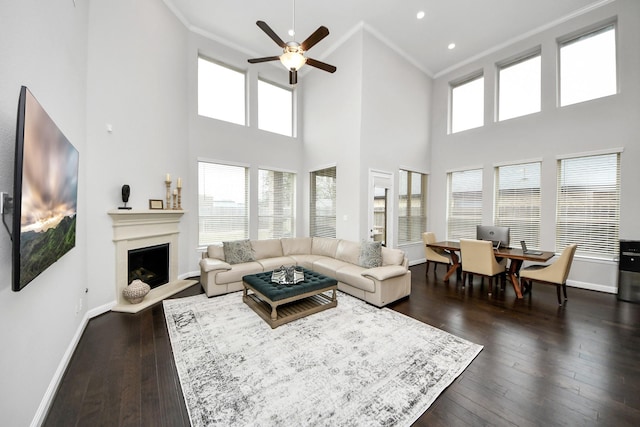 living room with dark hardwood / wood-style flooring, a towering ceiling, ornamental molding, and ceiling fan