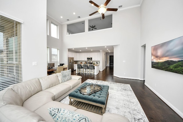 living room featuring ornamental molding, dark wood-type flooring, ceiling fan, and a towering ceiling