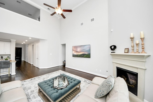 living room featuring crown molding, a towering ceiling, dark hardwood / wood-style flooring, and ceiling fan