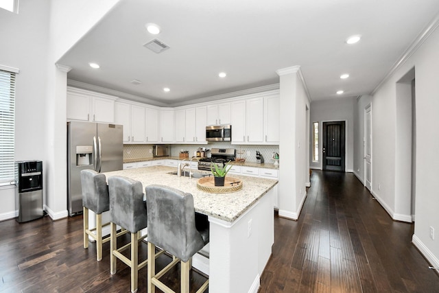 kitchen featuring a kitchen island with sink, light stone counters, white cabinets, and appliances with stainless steel finishes