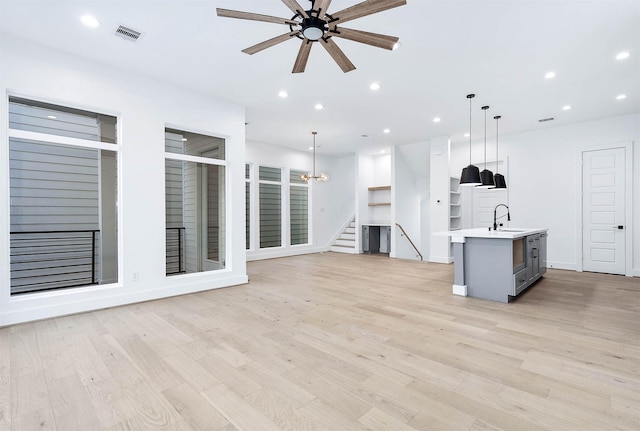 unfurnished living room featuring sink, ceiling fan with notable chandelier, and light hardwood / wood-style flooring