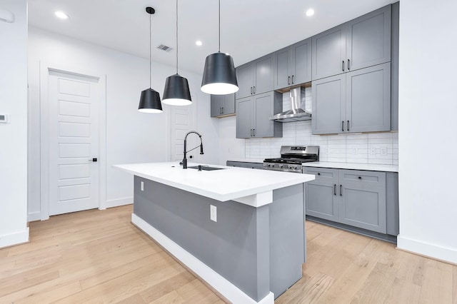 kitchen with sink, stainless steel gas stove, hanging light fixtures, wall chimney exhaust hood, and light wood-type flooring