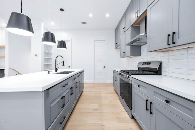 kitchen featuring wall chimney exhaust hood, sink, decorative light fixtures, stainless steel range with gas stovetop, and gray cabinets