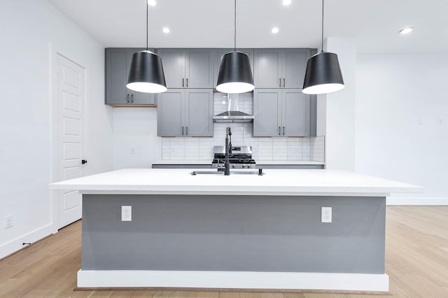 kitchen with gray cabinetry, pendant lighting, a center island with sink, and wall chimney range hood