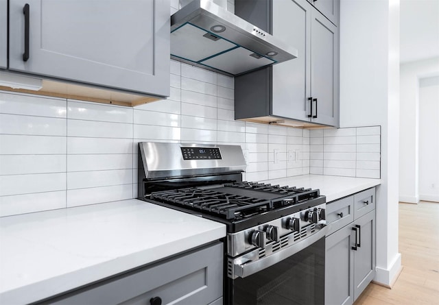 kitchen featuring gray cabinetry, backsplash, extractor fan, stainless steel range with gas cooktop, and light wood-type flooring