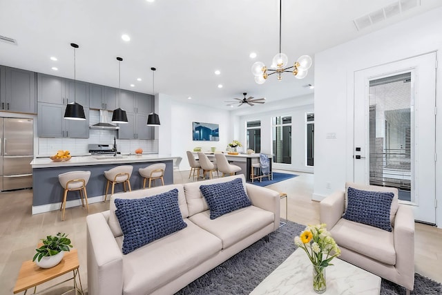 living room featuring ceiling fan with notable chandelier, sink, and light hardwood / wood-style flooring