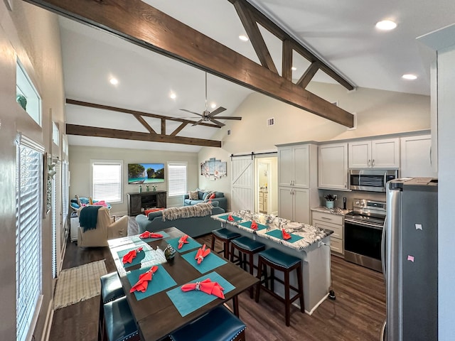 kitchen with a barn door, white cabinetry, appliances with stainless steel finishes, and vaulted ceiling with beams