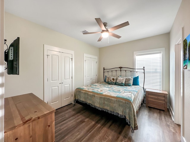 bedroom featuring ceiling fan, dark hardwood / wood-style flooring, and two closets