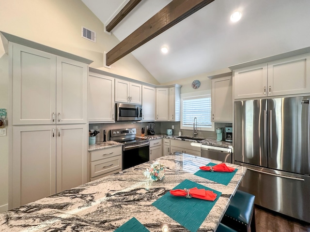 kitchen with white cabinets, appliances with stainless steel finishes, sink, and vaulted ceiling with beams