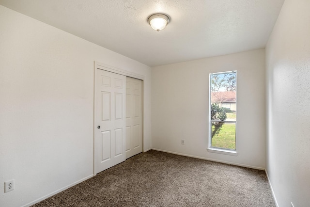 unfurnished bedroom featuring carpet floors, a textured ceiling, baseboards, and a closet