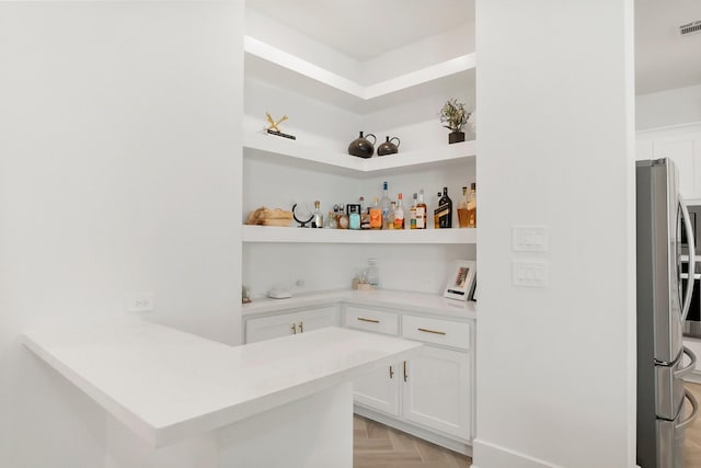 bar with light parquet flooring, stainless steel fridge, and white cabinets