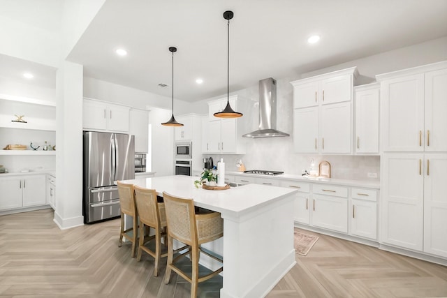 kitchen with white cabinets, a kitchen breakfast bar, wall chimney range hood, stainless steel appliances, and a center island with sink