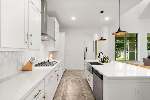 kitchen featuring sink, a kitchen island with sink, stainless steel appliances, white cabinets, and wall chimney exhaust hood