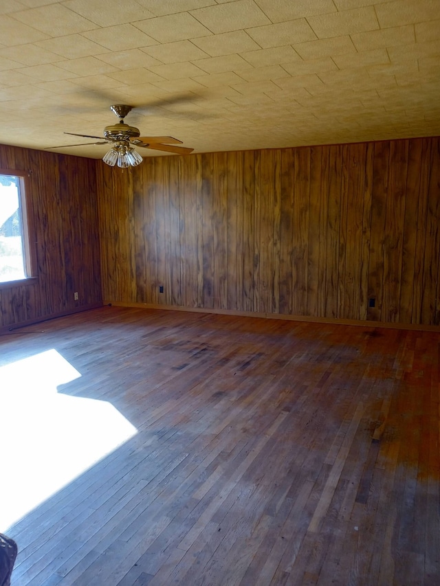 empty room featuring wooden walls, ceiling fan, and dark hardwood / wood-style flooring