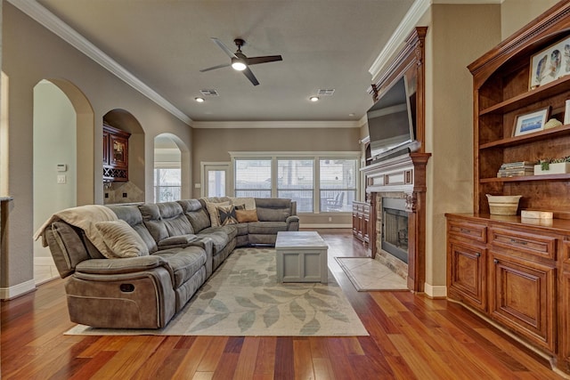 living room featuring light hardwood / wood-style flooring, ornamental molding, a tile fireplace, and ceiling fan