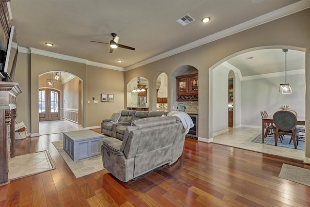 living room featuring hardwood / wood-style flooring, ornamental molding, ceiling fan with notable chandelier, and french doors