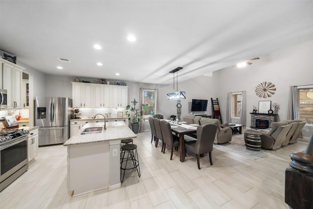 kitchen featuring sink, appliances with stainless steel finishes, a kitchen island with sink, a kitchen breakfast bar, and light stone countertops