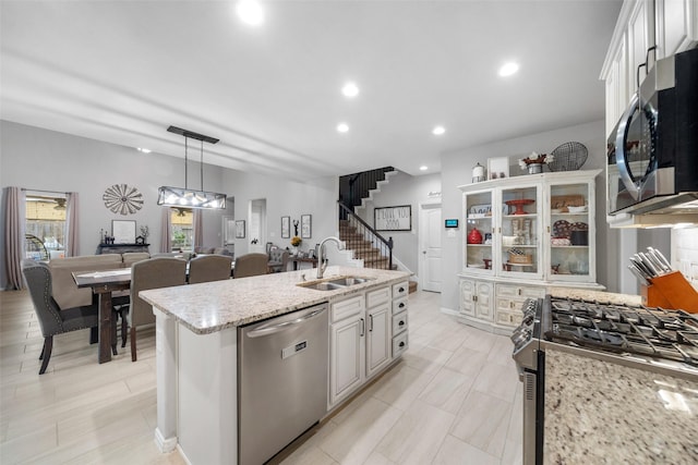 kitchen featuring sink, appliances with stainless steel finishes, pendant lighting, a kitchen island with sink, and white cabinets