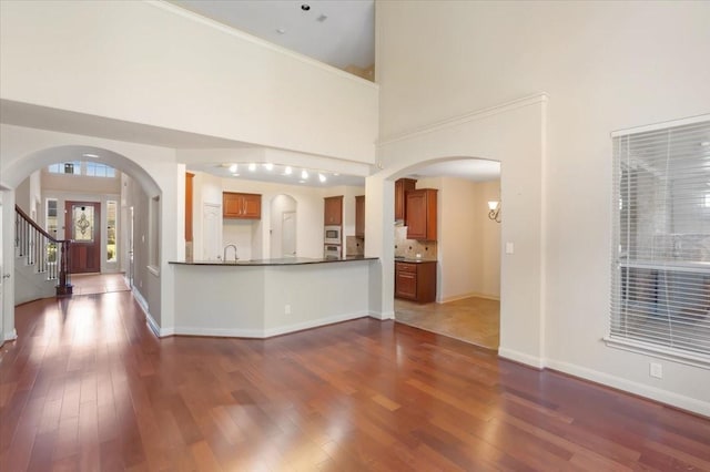 kitchen with dark wood-type flooring, sink, stainless steel microwave, kitchen peninsula, and a towering ceiling