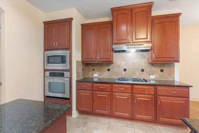 kitchen featuring backsplash, light tile patterned floors, stainless steel appliances, and dark stone counters