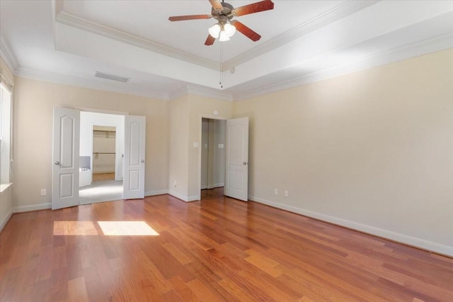 unfurnished bedroom featuring ceiling fan, ornamental molding, a tray ceiling, and light wood-type flooring