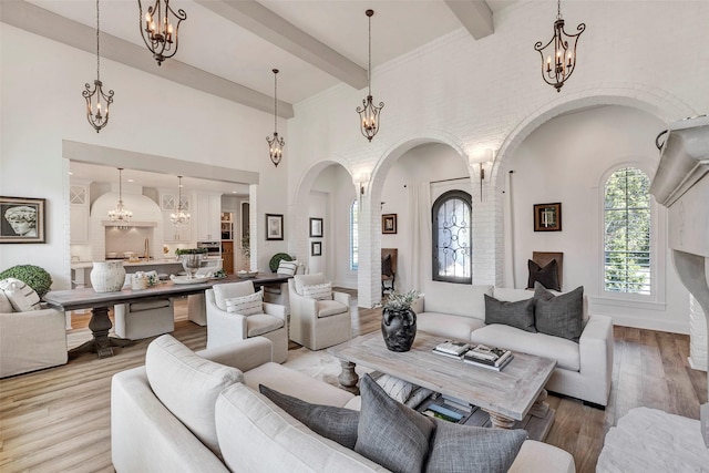 living room with wood-type flooring, beam ceiling, a chandelier, and a high ceiling