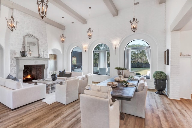 living room with beamed ceiling, a towering ceiling, a notable chandelier, and light hardwood / wood-style flooring