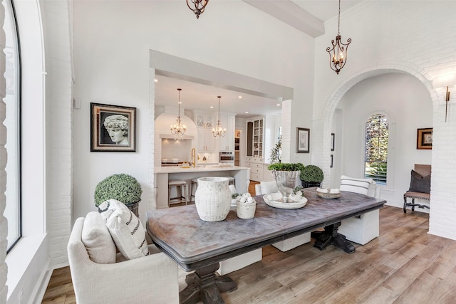 dining space featuring an inviting chandelier, sink, a high ceiling, and light wood-type flooring