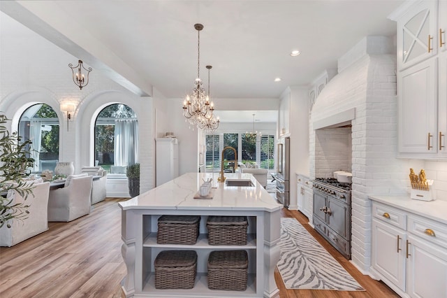 kitchen featuring sink, a chandelier, a center island with sink, pendant lighting, and white cabinets