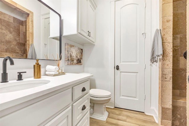 bathroom featuring wood-type flooring, toilet, vanity, and a tile shower