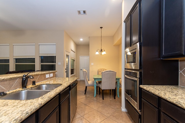 kitchen with sink, appliances with stainless steel finishes, light stone countertops, decorative backsplash, and decorative light fixtures