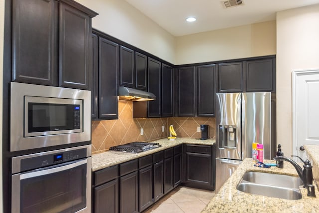 kitchen with stainless steel appliances, light stone countertops, sink, and backsplash